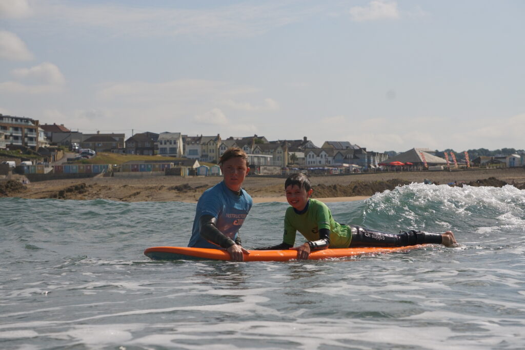 surfing lessons. young boy floating on a surfboard being helped by a surfing instructor.