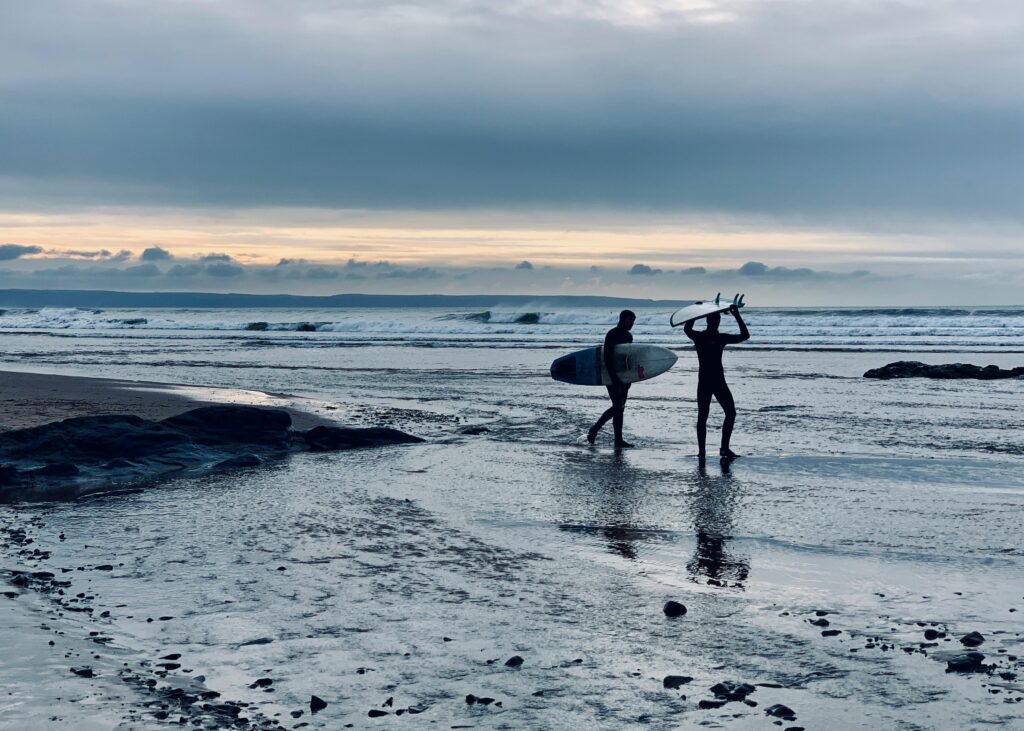 surfing cornwall uk. two surfers on the beach carrying their surfbaords