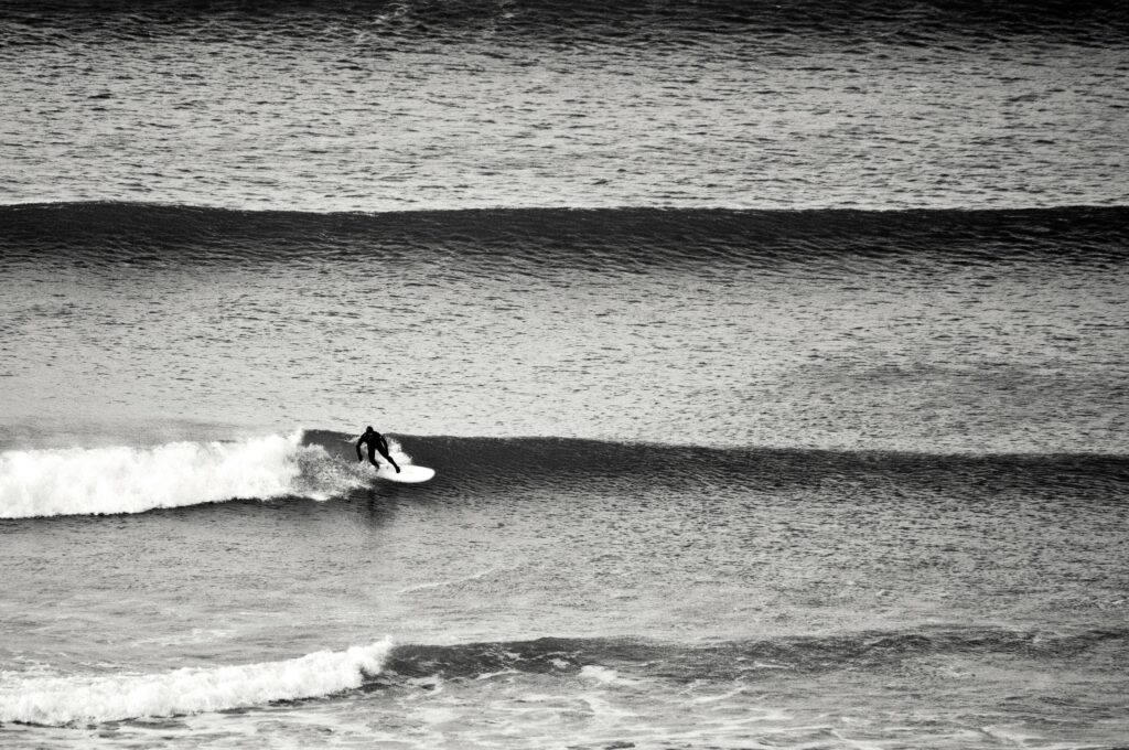 best place to surf in england. black and white photo of surfer riding an unbroken wave.