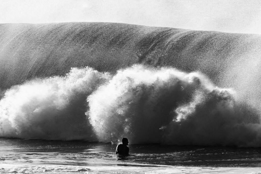 big wave surfing. Black and white photo of a big waves crashing as a man duck under it.