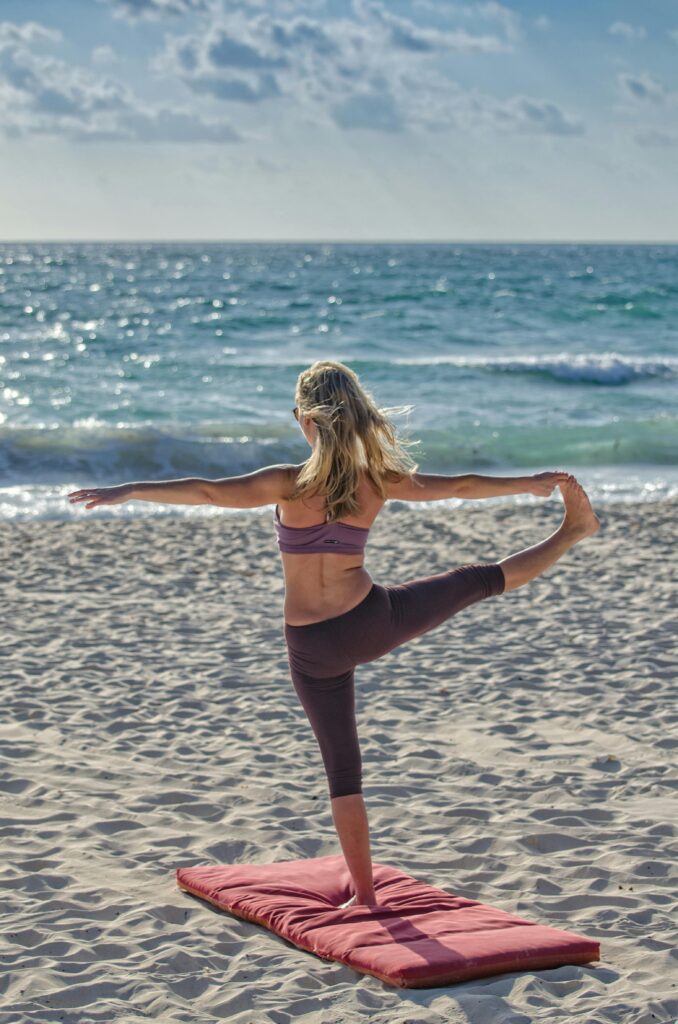 new surfing. woman doing a yoga pose on one leg while looking out to sea.