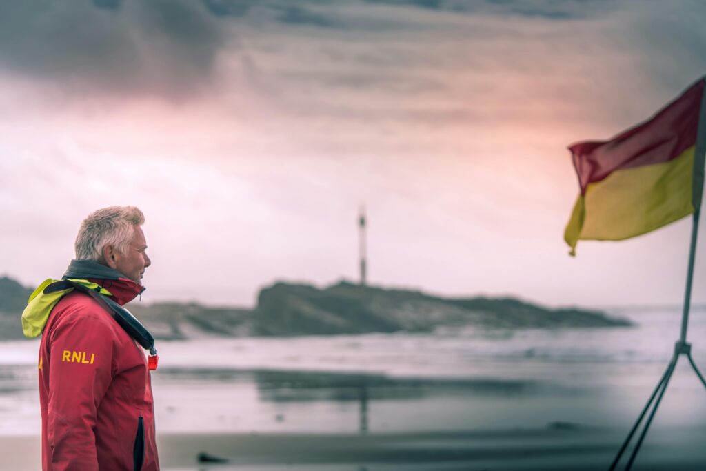 best surfing beach cornwall. lifeguard looks out to sea with red and yellow flag and barrel rock, summerleaze beach in the background.