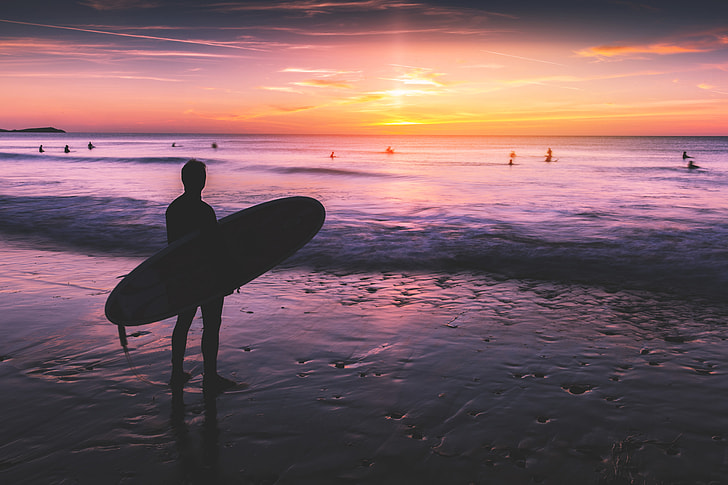 surfing lessons in bude. Surfer stand by the shore looking out at the sea with a sunset.