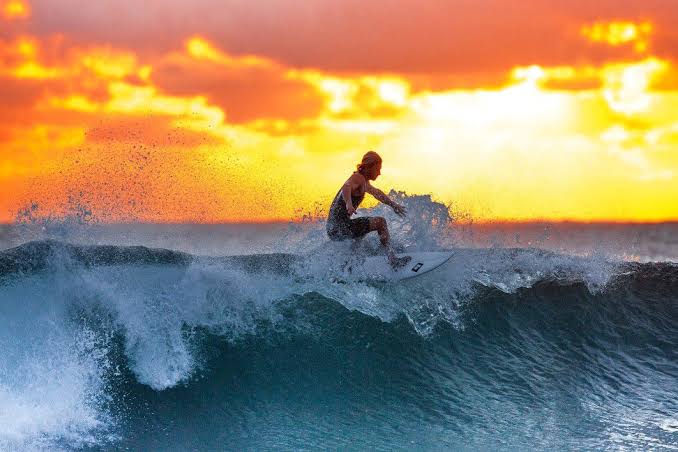 surfing course. surfer rides a wave with a setting sun behind.